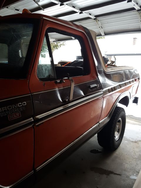 1978 Ford Bronco - Side view of a vintage orange and brown Ford Bronco Ranger XLT parked in a garage. The vehicle shows some wear and tear, with visible dents…