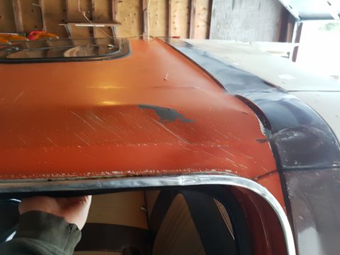 1978 Ford Bronco - A close-up view of the roof of an orange vehicle, showing peeling paint and scratches. A hand is visible gripping the edge of the roof.