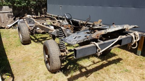 1978 Ford Bronco - This is a disassembled 1978 Ford Bronco chassis with suspension and tires. The frame is outdoors on grass, partially covered by a grey tarp.