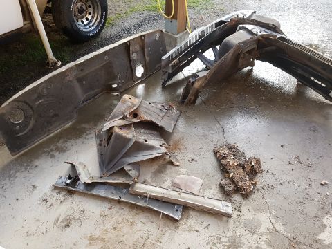 1978 Ford Bronco - Disassembled vehicle parts, including a large metal panel, a bent grille, and a pile of debris, are laid out on a wet concrete surface.