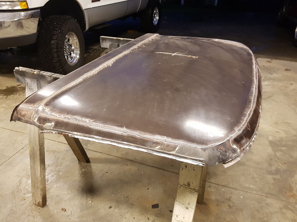 Bare metal truck hood resting on stands in a garage being worked on