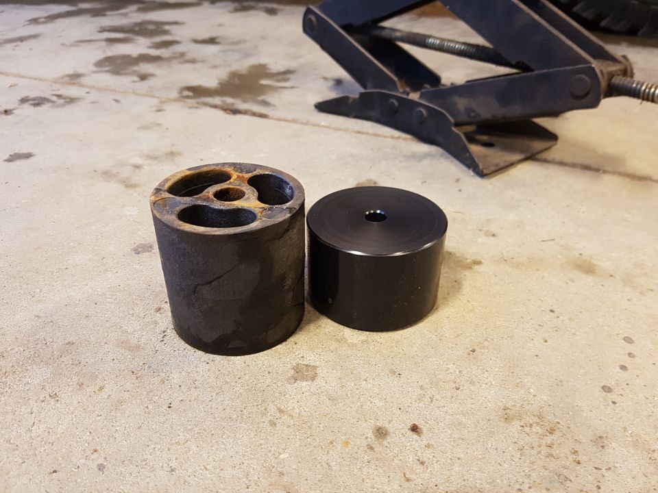 Two suspension lift blocks, one rusted and one black, on a concrete surface.