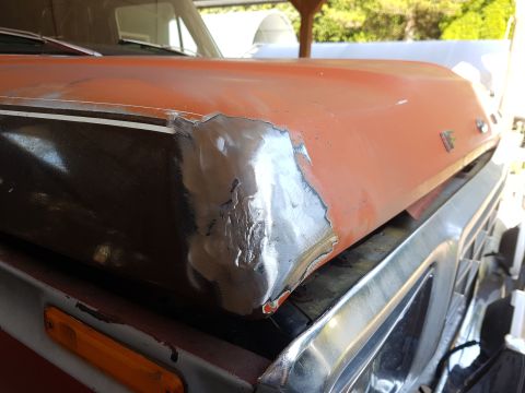 1978 Ford Bronco - A close-up, low-angle view of the front corner of an orange vehicle's hood, showing metal repair work. The vehicle appears to be a classic…