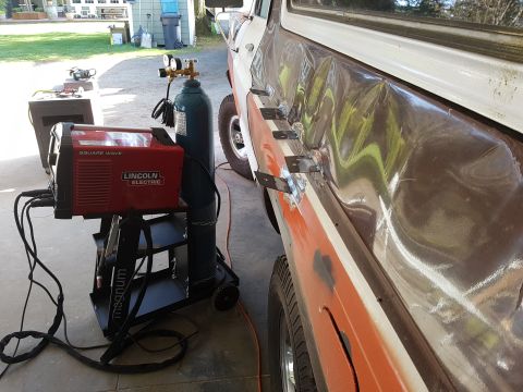 1978 Ford Bronco - A red Lincoln Electric Square Wave TIG welder and a green gas cylinder are set up next to a damaged brown and white vehicle, likely undergo…