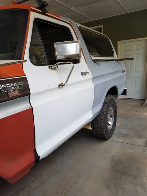 1978 Ford Bronco - The side profile of a Ford Bronco undergoing restoration shows a two-tone paint job with red on the front fender and door, and white and gr…