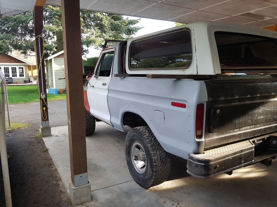 Rear passenger side view of a vintage Ford pickup truck in primer gray with a white camper shell.