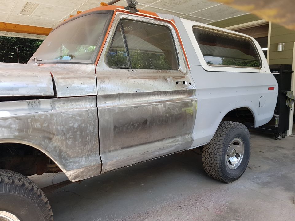 Classic Ford Bronco side view, primer and bare metal body panels, undergoing restoration.