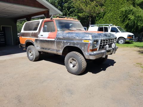 1978 Ford Bronco - A weathered, two-tone orange and white Ford Bronco is parked on a dirt driveway in front of a garage. The vehicle shows signs of modificati…