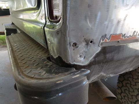 1978 Ford Bronco - A close-up view of the rear corner of a vehicle undergoing bodywork, showing bare metal, primer, and some rust repair. The diamond plate st…