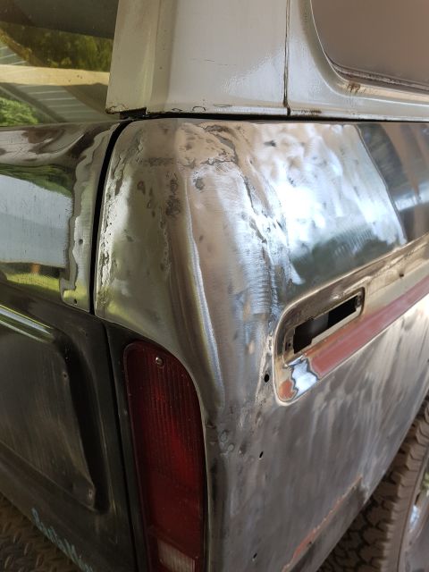 1978 Ford Bronco - A close-up, side-rear view of a vehicle's body panel that has been stripped to bare metal and appears to be undergoing repair or preparatio…