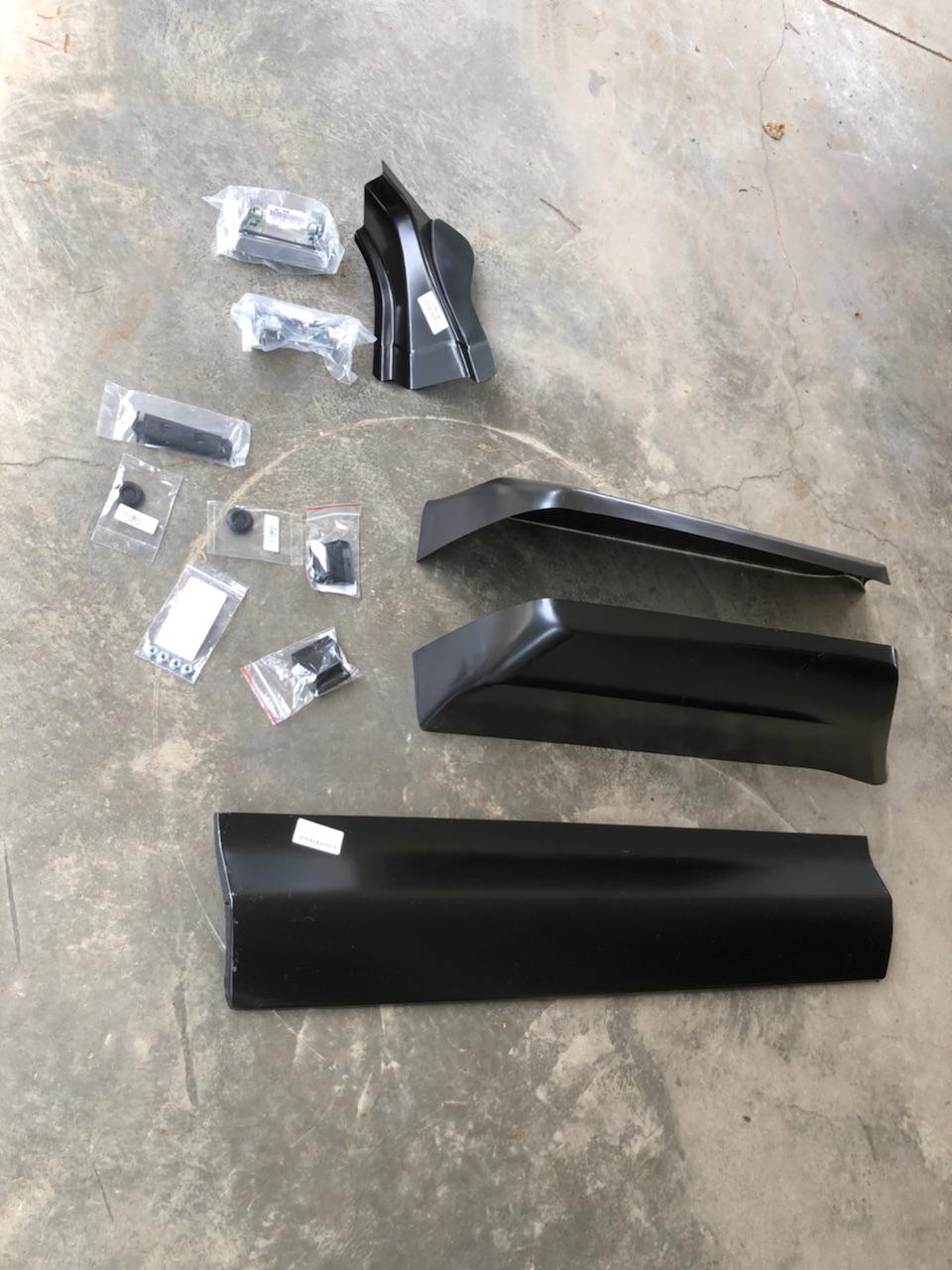 Black metal body panels and hardware parts for a vehicle on concrete.