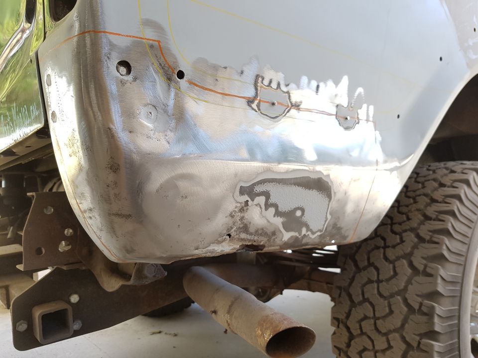 Close-up of a vehicle's rear quarter panel being prepped for body repair, showing stripped metal and repair marks.