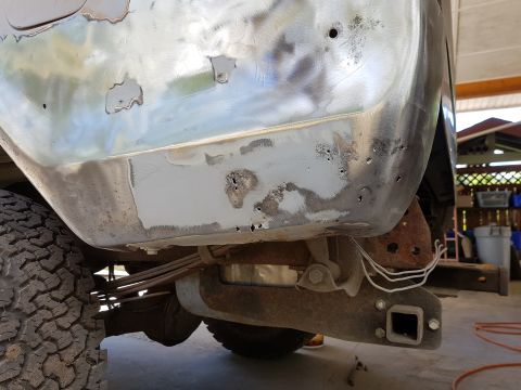 1978 Ford Bronco - The rear quarter panel of a vehicle is shown undergoing bodywork, with bare metal, primer, and rust visible. The suspension and tire are al…