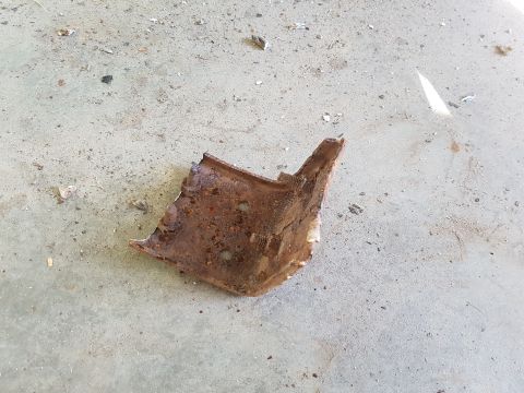 1978 Ford Bronco - A rusty, broken metal bracket with two visible bolt holes sits on a concrete surface scattered with debris.