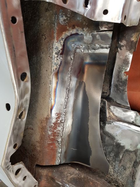 1978 Ford Bronco - Close-up view of freshly welded metal seams on the interior of a vehicle's body, showing colorful heat discoloration and some surface rust.