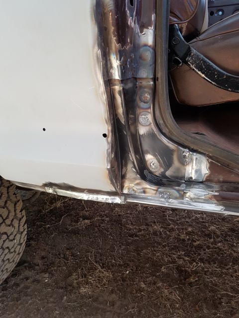 1978 Ford Bronco - Close-up view of the lower door jamb and rocker panel area of a vehicle undergoing repair. Welds and bare metal are visible, indicating bod…