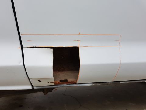 1978 Ford Bronco - A white vehicle door with a section cut out, revealing rusted metal underneath. Orange lines are drawn on the door, indicating repair or mo…