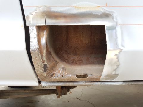 1978 Ford Bronco - A close-up view of a vehicle's lower body panel, showing significant rust damage and metal repair work. A large section of the panel has be…