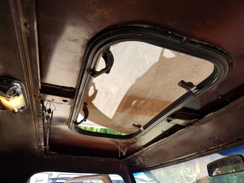 1978 Ford Bronco - The interior of a vehicle showing an open sunroof with a brown headliner and a chrome dome light.