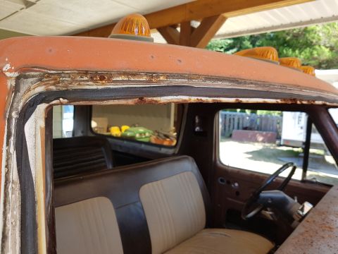 1978 Ford Bronco - Close-up view of the rusted top edge of a vintage truck cab, showing the window seal and orange roof lights. The interior features two-tone…