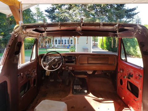 1978 Ford Bronco - The interior of a vintage Ford Bronco undergoing restoration, showing the dashboard, steering wheel, and door panels. The roof is disassemb…