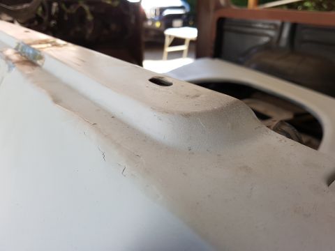 1978 Ford Bronco - A close-up, low-angle shot shows the weathered, light-colored painted surface of a vehicle's body panel, possibly a fender or hood, with vi…