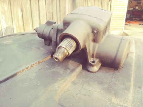 1996 Ford Bronco - A close-up, high-angle shot of a black steering gear box with a splined input shaft. The part is resting on a textured black surface with f…