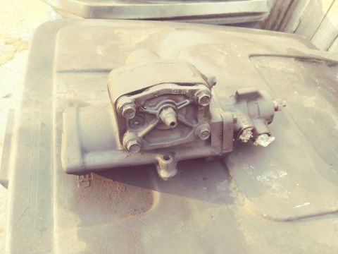1996 Ford Bronco - A close-up view of a power steering gearbox, likely for a 1996 Ford Bronco, resting on a dark surface. The part is black and shows signs of…