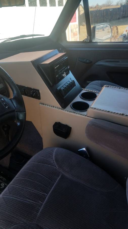 Interior of a Ford Bronco showing a custom center console with stereo, cup holders, and switches.