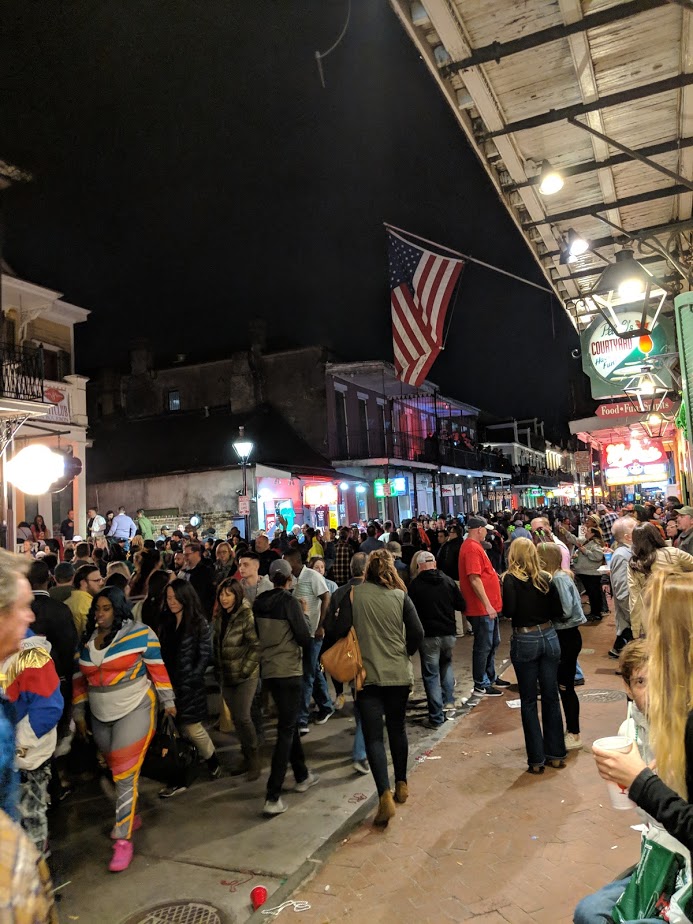 Crowded street at night with American flag overhead.