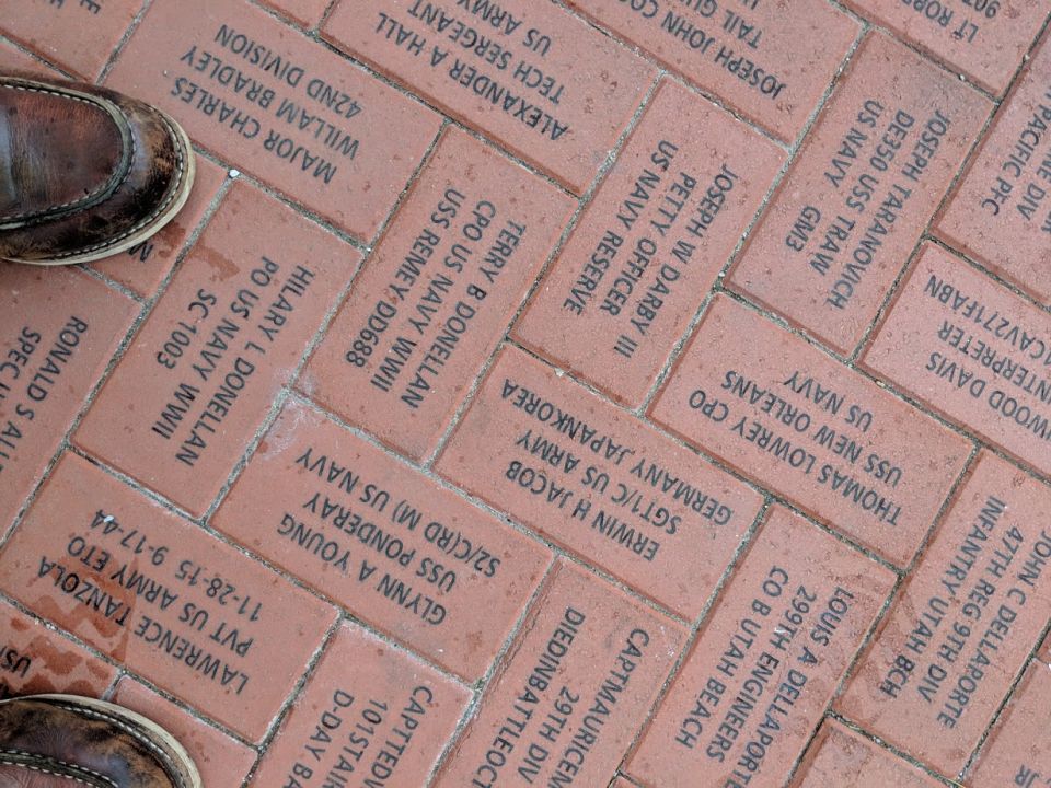 Engraved bricks with military names and service details on a walkway.