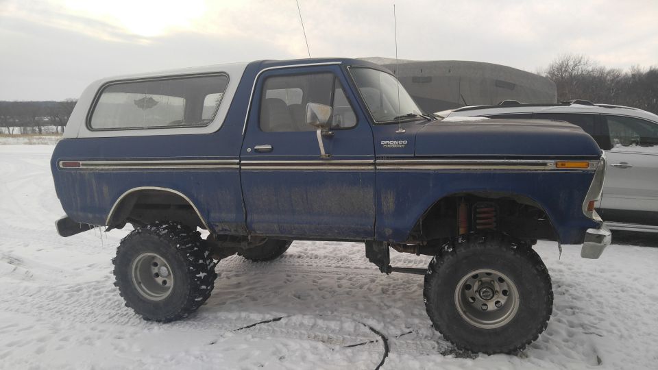 Lifted dark blue 1979 Ford Bronco with white top in a snowy field.