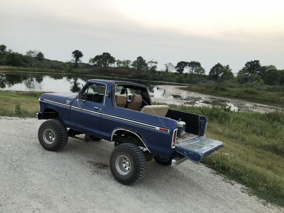 Lifted 1979 Ford Bronco parked by a lake with tailgate down.