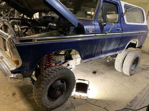 1979 Ford Bronco - A blue 1979 Ford Bronco with the hood open is parked in a garage, revealing its engine and suspension modifications. The vehicle features d…