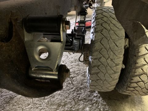 1979 Ford Bronco - A close-up, low-angle view of the rear suspension and tire assembly of a vehicle, likely a truck or SUV. Visible components include a leaf…