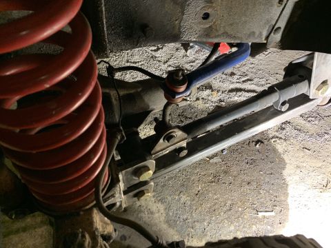 1979 Ford Bronco - A close-up view of the suspension system of a 1979 Ford Bronco, featuring a red coil spring, a blue sway bar, and a dark-colored adjustable…