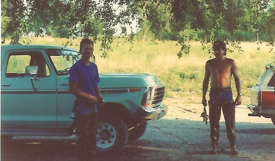 Two men by a vintage light blue Ford pickup truck and a red and silver SUV.
