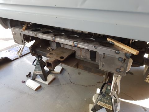 1978 Ford Bronco - A custom metal bumper assembly with circular cutouts is mounted to the rear of a vehicle, supported by jack stands. The assembly appears to…