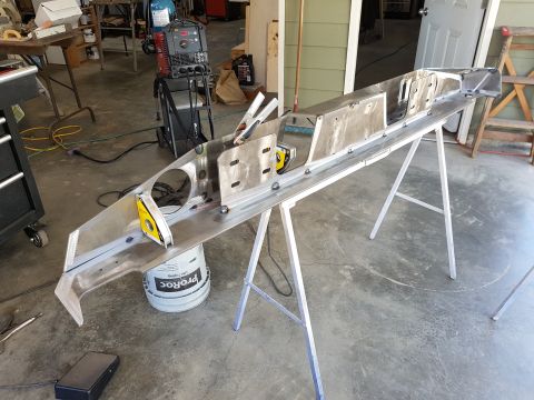 1978 Ford Bronco - A custom metal fabrication project, possibly a chassis or frame, is shown in a workshop setting. The long, angular piece of metal is suppor…