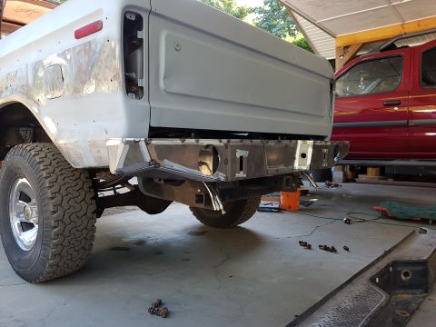 1978 Ford Bronco - The rear passenger side of a light gray Ford Bronco is shown, undergoing modifications. A custom steel bumper is installed, and the vehicle…