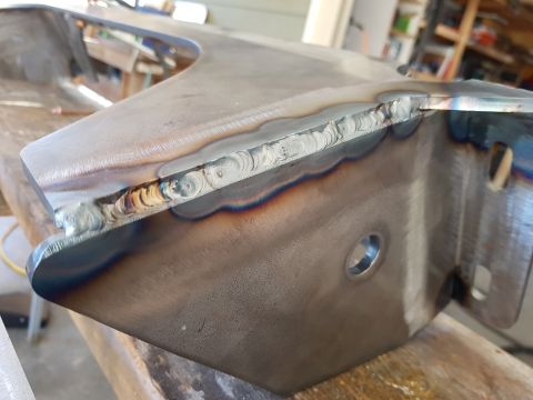 1978 Ford Bronco - A close-up shot shows a metal automotive part with visible welding seams and heat discoloration. The part has several holes and appears to…