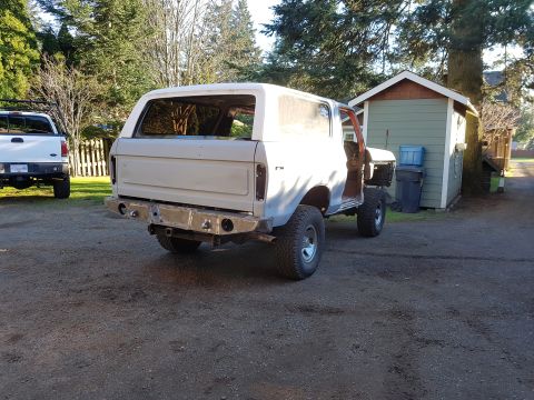 1978 Ford Bronco - A 1978 Ford Bronco in primer sits in a driveway next to a shed, with a white pickup truck in the background.