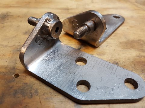 1978 Ford Bronco - Close-up of two custom metal brackets with bolts, resting on a wooden surface.