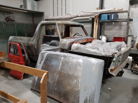 1978 Ford Bronco - Unfinished Ford F-Series truck body in a workshop, showing primer and some rust. A red door is detached.