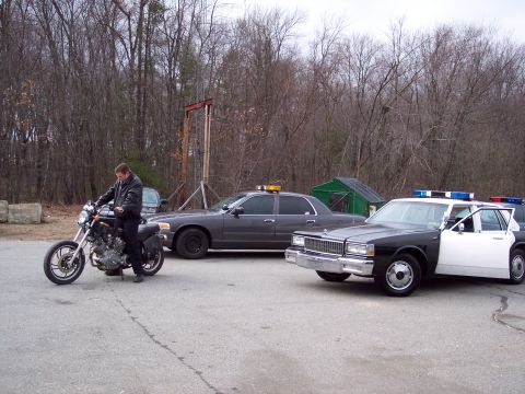 2001 Ford Crown Victoria - A man sits on a motorcycle with two police cars in the background.