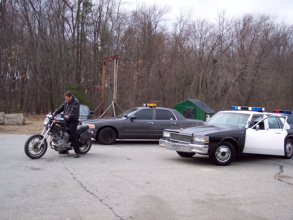 Man on motorcycle parked next to a dark police car and a black and white police car with doors open