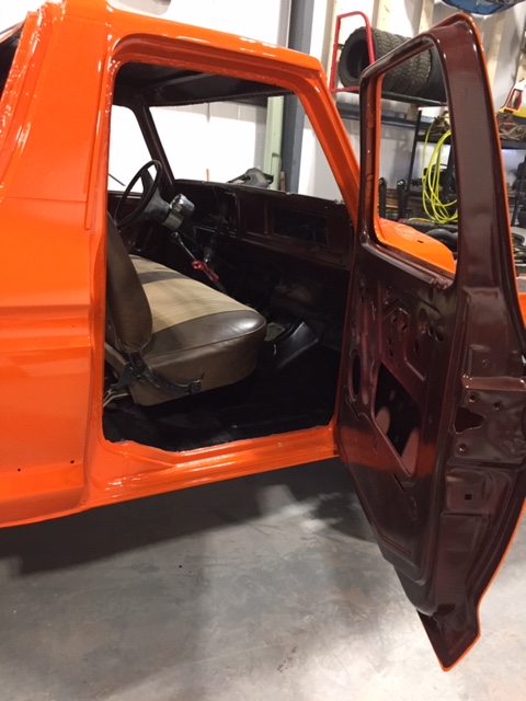 1978 Ford Bronco - The interior of an orange pickup truck is shown with the driver's side door open, revealing the seats and dashboard.