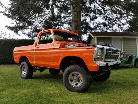1978 Ford Bronco - This orange pickup truck is parked on a grassy lawn in front of a house, with its hood open.