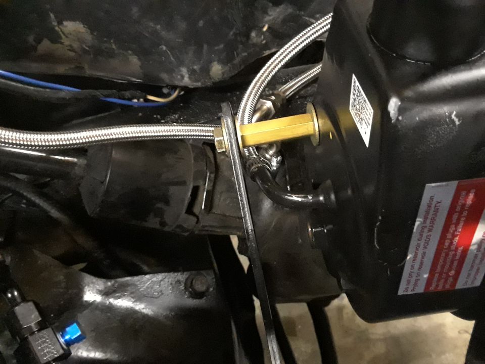 Close-up of power steering pump with braided lines and brass fittings. Text on a red warning sticker is visible