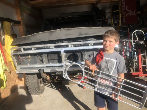 1978 Ford Bronco - A young boy holds a Ford grille in front of a truck that appears to be undergoing restoration.